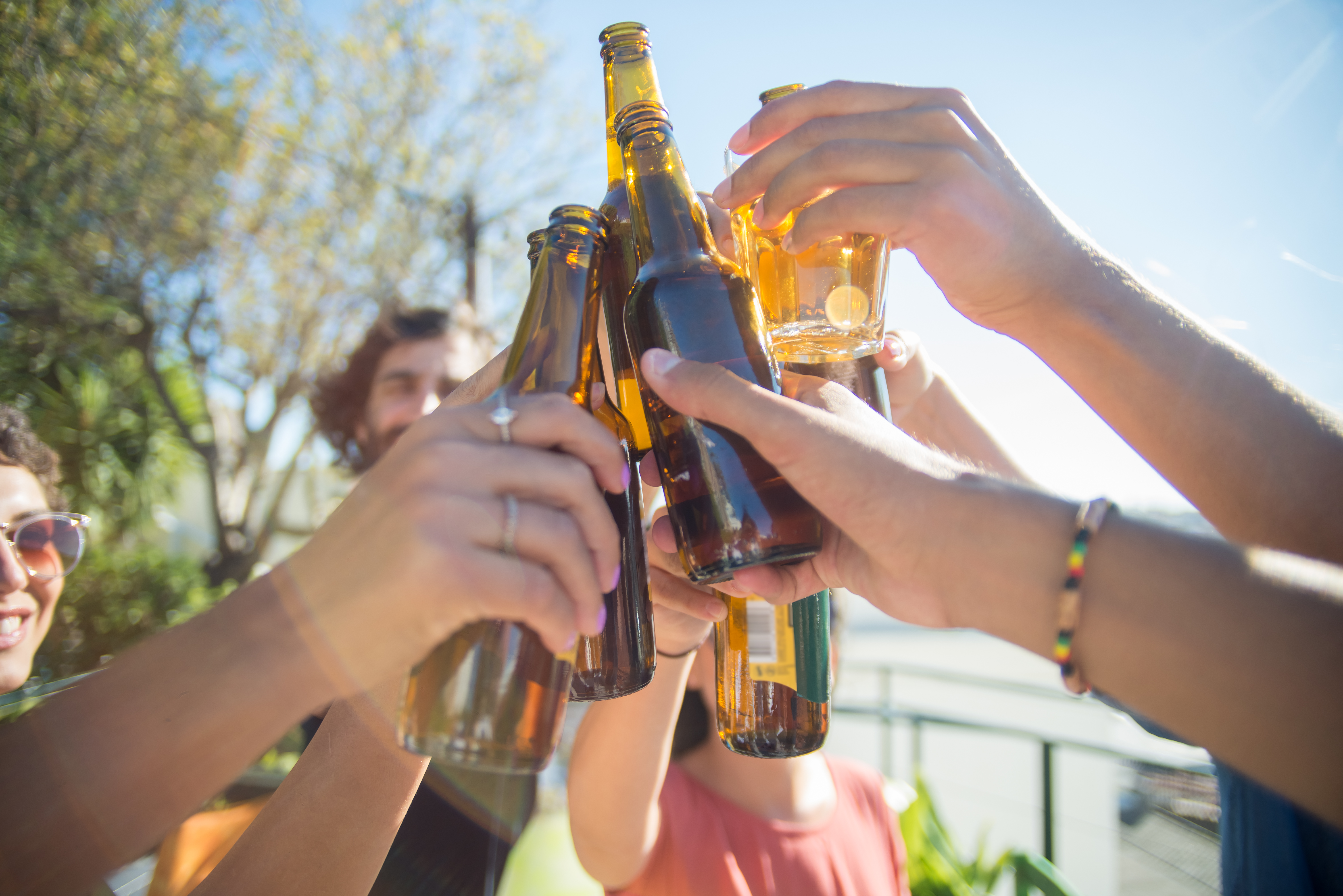 Close-up of content friends clinking beer bottles and glasses